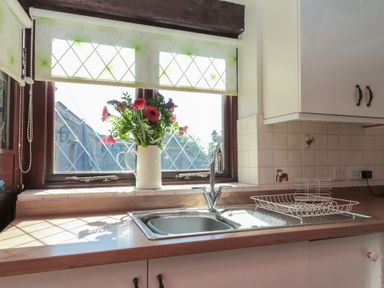A kitchen sink with a dish rack and a vase of flowers on the windowsill at Beaconsfield Cottage in Burniston near Scalby