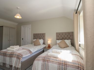A bedroom with two single beds a nightstand with a lamp and a wardrobe at Beaconsfield Cottage in Burniston near Scalby