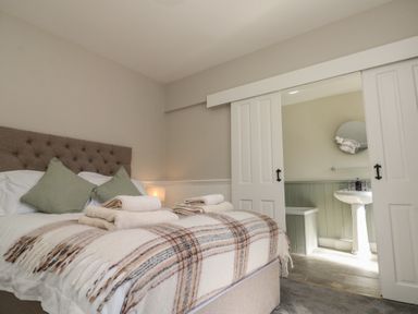 A bedroom with a bed covered in a plaid blanket and towels with an adjoining bathroom visible through sliding doors at Beaconsfield Cottage in Burniston near Scalby