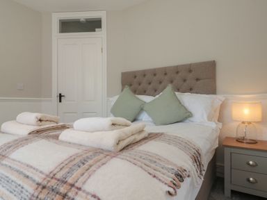 A bedroom with a bed with folded towels pillows a lamp on a bedside table and a closed white door at Beaconsfield Cottage in Burniston near Scalby
