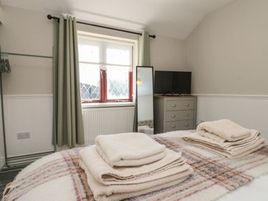 A bedroom with folded towels on bed a window with curtains a mirror a chest of drawers and a television at Beaconsfield Cottage in Burniston near Scalby