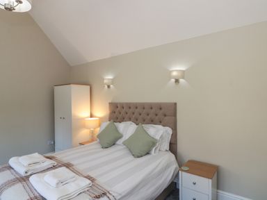 A bedroom with a double bed two green cushions bedside tables lamps and a white wardrobe at Beaconsfield Cottage in Burniston near Scalby