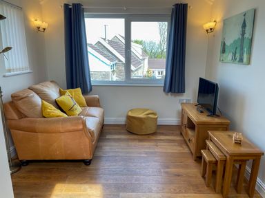 A living room with a leather sofa with yellow cushions a TV on a wooden stand and nested wooden tables at Pen- y- Bryn @ Canllefaes in Penparc near Cardigan