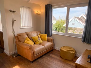 A living room with a brown leather sofa with yellow cushions a yellow pouf a floor lamp and a window with grey curtains at Pen- y- Bryn @ Canllefaes in Penparc near Cardigan