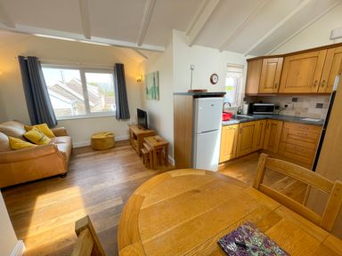 A living room with a sofa and a television next to a kitchen with wooden cabinets and a dining table at Pen- y- Bryn @ Canllefaes in Penparc near Cardigan