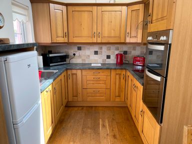 A kitchen with wooden cabinets a white refrigerator a microwave a red kettle a red toaster and an oven at Pen- y- Bryn @ Canllefaes Penparc near Cardigan