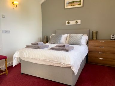 A bedroom with a double bed with gray pillows and folded towels a wooden dresser and red carpet at Pen- y- Bryn @ Canllefaes Penparc near Cardigan