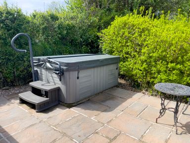 An outdoor patio area with a covered hot tub with steps and a small round metal table surrounded by green bushes at Pen- y- Bryn @ Canllefaes in Penparc near Cardigan