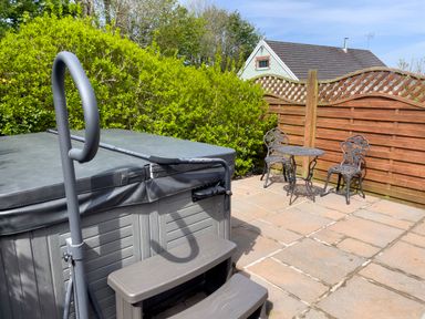 An outdoor patio area with a covered hot tub and plastic steps next to a metal table and two chairs by a wooden fence and green bushes at Pen- y- Bryn @ Canllefaes in Penparc near Cardigan