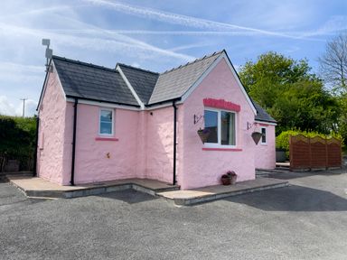 A pink painted house with flower pots hanging outside next to a paved area and trees at Pen- y- Bryn @ Canllefaes Penparc near Cardigan