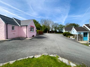 A paved driveway with a pink house on the left and blue houses on the right with trees in the background at Pen- y- Bryn @ Canllefaes in Penparc near Cardigan