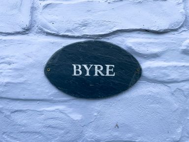 A black oval sign with the word BYRE on a white textured wall at The Byre @ Canllefaes Penparc near Cardigan