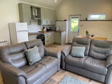 A kitchen and living area with two gray leather sofas and kitchen cabinets at The Byre @ Canllefaes in Penparc near Cardigan