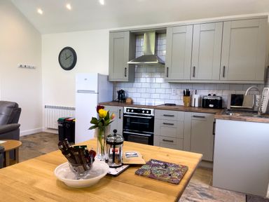 A kitchen with gray cabinets white fridge oven and a wooden table with flowers and a coffee press at The Byre @ Canllefaes in Penparc near Cardigan