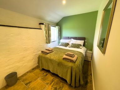 A bedroom with a double bed covered with green bedding and towels on it a window with green curtains and a mirror on the wall at The Byre @ Canllefaes in Penparc near Cardigan