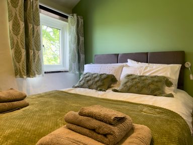 A bedroom with a bed with green pillows and blanket and towels on the bed near a window at The Byre @ Canllefaes in Penparc near Cardigan