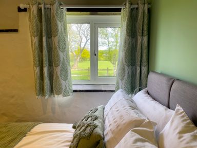 A bedroom with a window and patterned curtains and a bed with pillows and a blanket at The Byre @ Canllefaes in Penparc near Cardigan