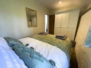 A bedroom with a bed with pillows and folded towels next to a wardrobe and a mirror on the wall at The Byre @ Canllefaes in Penparc near Cardigan