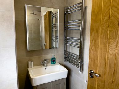 A bathroom with a sink cabinet mirror towel radiator and wooden door at The Byre @ Canllefaes in Penparc near Cardigan