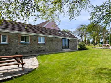 A yard with a lawn picnic table stone patio and a stone building with windows and doors at The Byre @ Canllefaes in Penparc near Cardigan