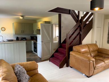 A living room with two brown leather sofas next to a staircase and an open door leading to a kitchen at The Shippen @ Canllefaes in Penparc near Cardigan