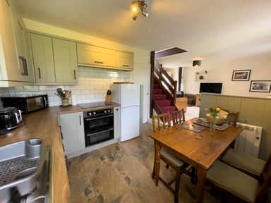A kitchen with wooden dining table and chairs, appliances, and a staircase leading to a living area at The Shippen @ Canllefaes in Penparc near Cardigan