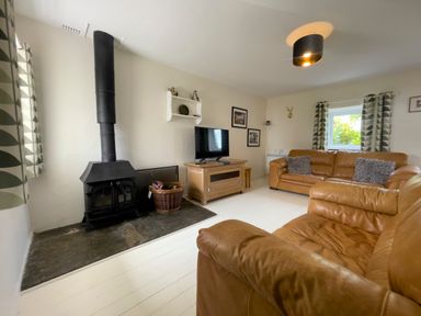 A living room with leather sofas a wood stove a television and patterned curtains at The Shippen @ Canllefaes in Penparc near Cardigan