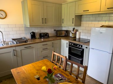 A kitchen with white cabinets and wooden countertops a wooden table with flowers and chairs a white refrigerator and black appliances at The Shippen @ Canllefaes Penparc near Cardigan