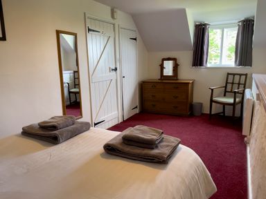 A bedroom with a bed with folded towels a dresser with a small mirror a wooden chair a window with curtains and two white doors at The Shippen @ Canllefaes Penparc near Cardigan