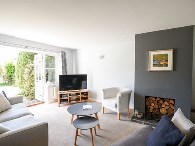 A living room with a sofa armchair round nesting tables TV and a fireplace stocked with firewood at 12 The Gardens in Rousdon