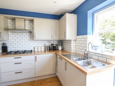 A kitchen with white cabinets and wooden countertops a stainless steel sink and a gas stove at 12 The Gardens in Rousdon
