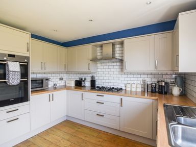 A kitchen with white cabinets wooden countertops a gas stove microwave and various kitchen appliances at 12 The Gardens in Rousdon