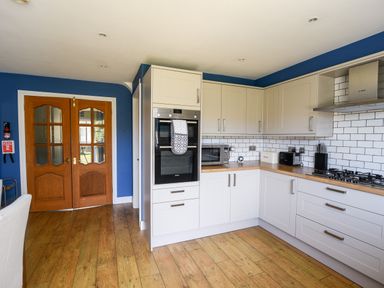 A kitchen with wooden floor white cabinets blue walls and wooden double doors at 12 The Gardens in Rousdon