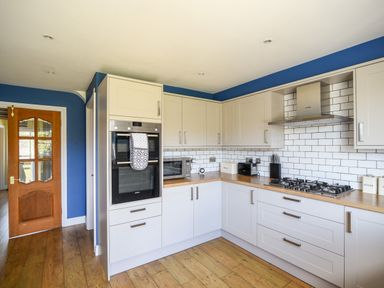 A kitchen with white cabinets wooden countertops a gas stove an oven a microwave and blue walls at 12 The Gardens in Rousdon