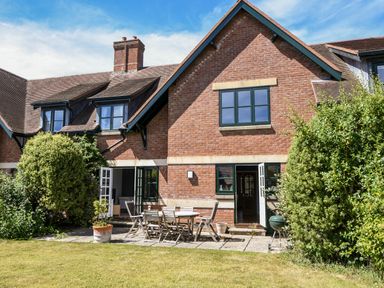 A brick house with black framed windows a patio table and chairs and green bushes at 12 The Gardens in Rousdon