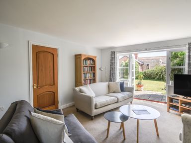 A living room with sofas a wooden door a bookcase a TV and glass doors leading to a garden at 12 The Gardens in Rousdon