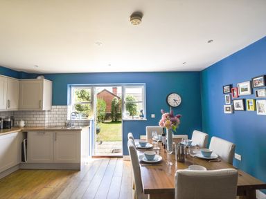 A kitchen and dining area with blue walls a wooden table set with dishes and a vase of flowers at 12 The Gardens in Rousdon