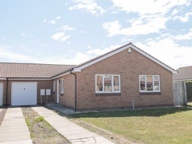 A single-story brick house with a tiled roof two windows a garage and a driveway at 20 Southmead in Amble
