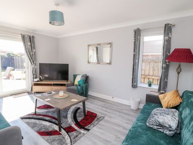A sitting room with a sofa, armchair, coffee table, television, and windows at 20 Southmead in Amble
