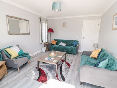 A living room with two green sofas one grey armchair and a wooden coffee table at 20 Southmead in Amble