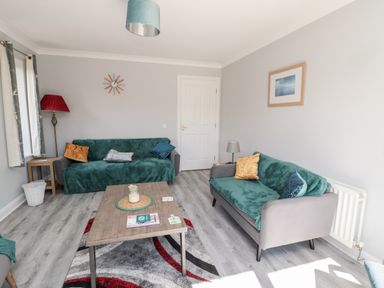 A living room with two sofas a wooden coffee table a floor lamp and a wall clock at 20 Southmead in Amble
