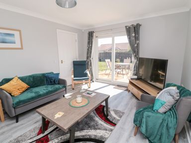 A living room with sofas chairs coffee table and television with sliding glass doors to a garden at 20 Southmead in Amble