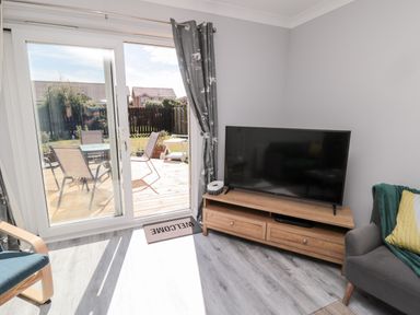 A living room with a television on a wooden stand near sliding glass doors opening to a patio at 20 Southmead in Amble
