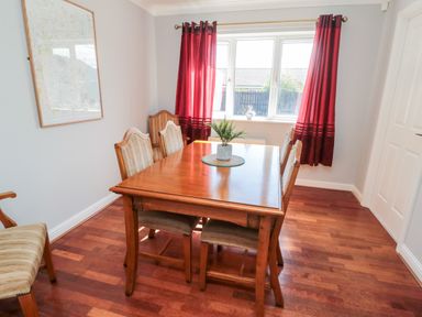 A dining room with a wooden table and chairs near a window with red curtains at 20 Southmead in Amble
