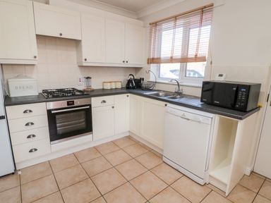 A kitchen with white cabinets tiled floor oven stove dishwasher and microwave at 20 Southmead in Amble
