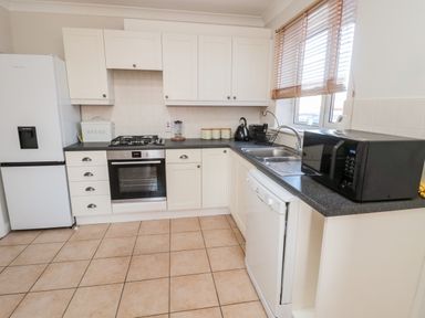 A kitchen with white cabinets a refrigerator an oven a dishwasher a microwave and a window with blinds at 20 Southmead in Amble