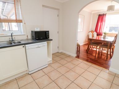 A kitchen area with a dishwasher microwave sink and a view of a dining room with red curtains at 20 Southmead in Amble