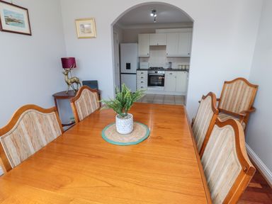 A dining area with a wooden table and upholstered chairs and a kitchen visible through an archway at 20 Southmead in Amble