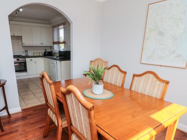 A dining room with a wooden table and six chairs next to an open archway leading to a kitchen at 20 Southmead in Amble