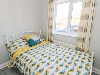 A bed with bird patterned bedding next to a window with patterned curtains at 20 Southmead in Amble